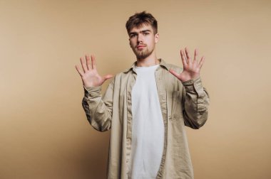 Elleri bej bir arkaplan üzerinde gündelik giyinmiş genç bir adam..