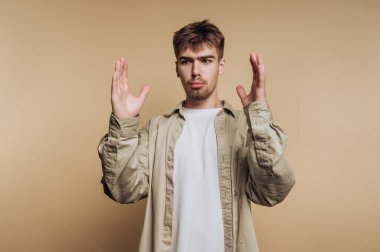 Kafası karışmış genç bir adam, elleri havada, bej bir geçmişi var..