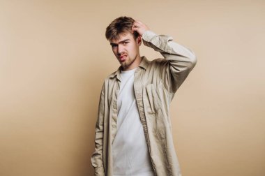 Günlük giysiler içinde kafasını kaşıyan genç bir adam, kafası karışmış bir ifade..