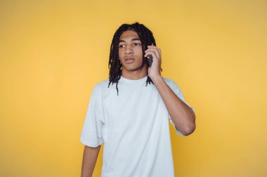 Örgülü genç adam sarı arka planda akıllı telefondan konuşuyor..