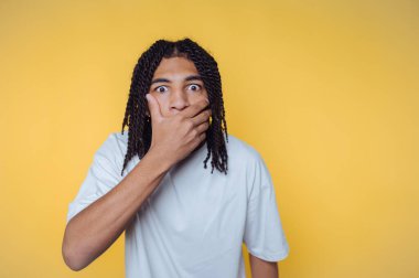 Şaşırmış genç bir adam, ağzı açık, sarı arka planda..