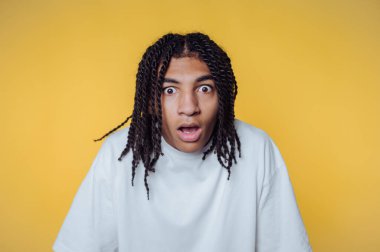 Sarı arka planda örgülü saçları olan şaşırmış genç bir adam..