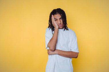 Beyaz gömlekli genç adam sarı arka planda sıkılmış görünüyor..