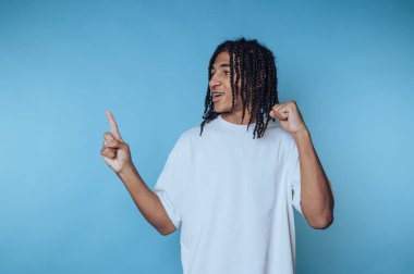 Saçları örgülü genç adam mavi arka plana bakıp gülümsüyor..