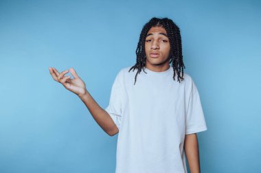 Beyaz tişörtlü, örgülü saçlı, mavi arka planda omuz silken genç bir adam..