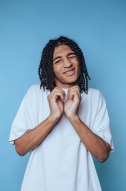 Saçları örgülü, göz kırpan ve gülümseyen genç bir adam..