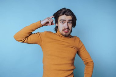 Turuncu kazaklı genç adam mavi arka planda kafası karışmış görünüyor..