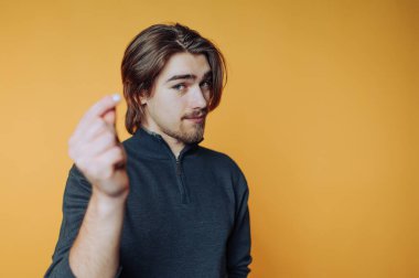 Uzun saçlı genç adam turuncu arka planda küçük bir nesne tutuyor..