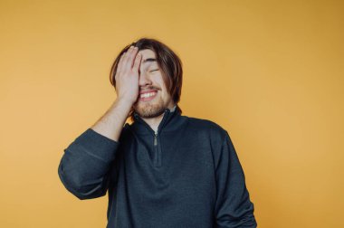 Uzun saçlı ve sakallı bir adam, sarı arka planda el ele gülümsüyor..