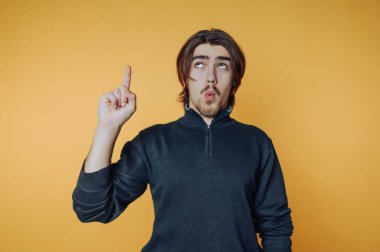 Uzun saçlı genç adam turuncu arkaplanı işaret ediyor..