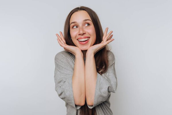 A cheerful woman with long hair smiling and holding her face.