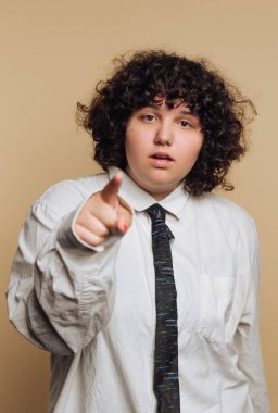 Büyük boy beyaz gömlek ve siyah kravat giymiş kıvırcık saçlı bir birey işaret ederek dikkatleri üzerine çeker. Tarafsız arka planlar, kendilerine güvenlerini vurguluyor..