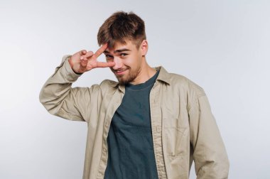 Genç bir adam barış işaretiyle neşeli bir poz verir, günlük kıyafetler giyer. Yüzündeki ifade, basit bir geçmişe karşı dostluk ve yakınlık gösteriyor..