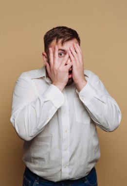 Delikanlının portresi bir şok anında çekilir, ellerini bej arka planda saklar.