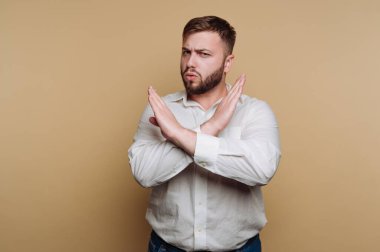 Kararlı bir gencin portresi güçlü bir reddetmeyi göstermek için kollarını kavuşturur. Bu da bej arkaplana güveni yansıtır.