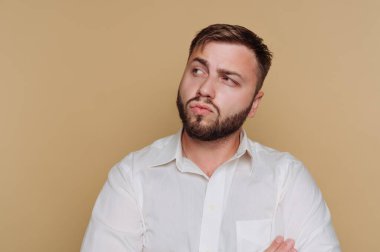 Düşünceli genç adamın portresi kameradan dışarı bakıyor, bej arka planda anlamlı bir şey yansıtıyor.