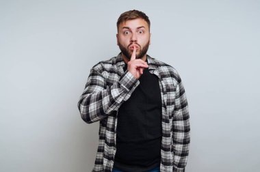 Genç bir adamın portresi sessizce sessiz sedasız hareket eder. Beyaz arka planda dudaklarına bir parmak yerleştirir.