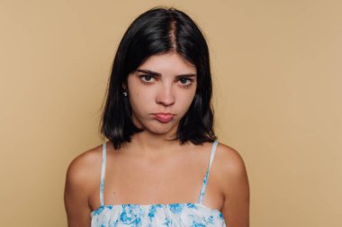 Genç bir kadının portresi somurtkan ve çatık kaşlı, bej arka plandaki hoşnutsuzluğu ve tefekkürü tasvir eden