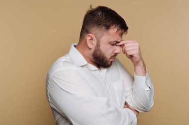 Beyaz gömlekli, ciddi görünüşlü genç bir adamın portresi bej arka plan üzerinde düşünürken hayal kırıklığını ifade eder.