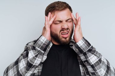 Genç bir adamın portresi hayal kırıklığı yaşar, başını tutar ve beyaz arka planda yüzünü buruşturur.