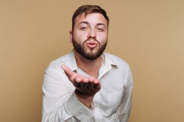 Çekici genç bir adamın portresi kameraya doğru bir öpücük yolluyor. Bej arka planda sıcaklığı ve sevgiyi yansıtıyor.