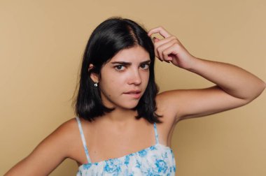 Kafası karışmış genç bir kadının portresi, bej arka plandaki merakı ya da tefekkürü yansıtıyor.