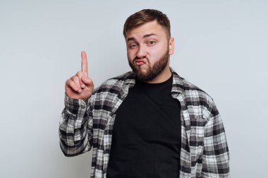 Şakacı bir ifadeyle genç bir adamın portresi beyaz arka planda önemli bir noktayı vurgular gibi parmağını kaldırır.