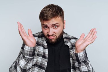 Genç adamın portresi omuz silkme ve şüpheci bir ifadeyle, beyaz arka planda bir belirsizlik anını yakalıyor.