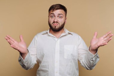 Kafası karışmış genç bir adamın portresi bej arka planda kafa karışıklığı ve belirsizlik taşıyor.