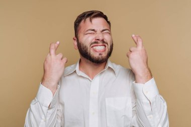 Neşeli ve umut dolu bir ifadeyle genç bir adamın portresi, parmakları bej arka planda.