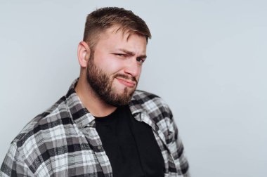 Sakallı genç bir adamın portresi, beyaz arka planda merak ve çekicilik taşıyan neşeli bir sırıtış sergiliyor.