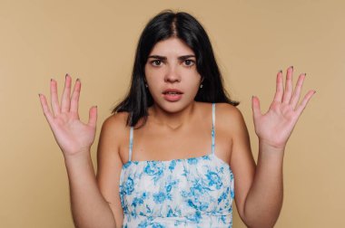 Bej arka planda ellerini kaldırarak şaşıran genç bir kadının portresi.