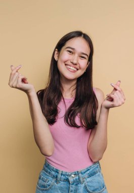 Pembe bluzlu, gülümseyen genç bir kadın parmak kalp hareketleri yapıyor..