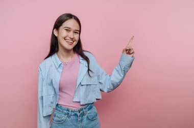 Gülümseyen genç bir kadın pembe bir arka plana işaret ediyor.