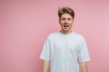 Beyaz tişörtlü genç adam pembe arka planda gülümsüyor..