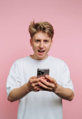 Beyaz tişörtlü genç adam elinde akıllı telefon, pembe arka plan.