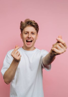 Beyaz tişörtlü genç adam parmaklarıyla kalp hareketi yapıyor..