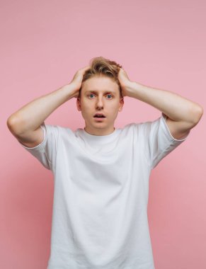 Pembe arka planda beyaz tişörtlü, şaşırmış bir genç..