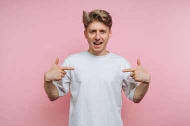 Beyaz tişörtlü genç adam pembe arka planda kendini gösteriyor..