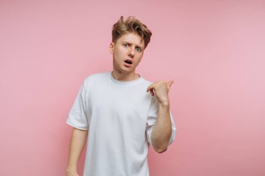 Beyaz tişörtlü genç adam şaşırmış görünüyor, pembe arka plan.