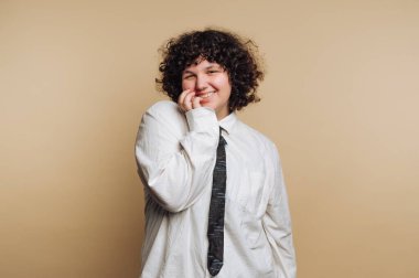 Beyaz gömlekli ve kravatlı, bej arka planda gülümseyen biri..