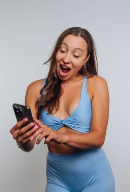 Mavi giysili kadın akıllı telefona şaşırmış görünüyor.