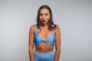 Gri arkaplan karşısında şaşırmış bir ifadeyle mavi elbiseli kadın..