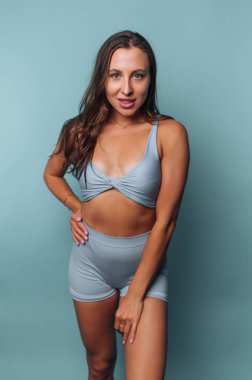 Mavi takım elbiseli kadın mavi arka planda poz veriyor..