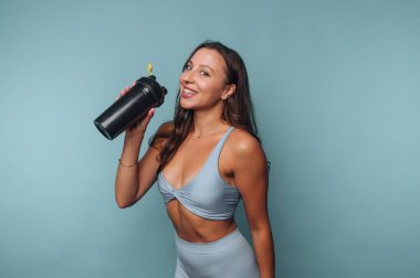 Antrenman kıyafetli bir kadın mavi arka planda bir şişe tutuyor..