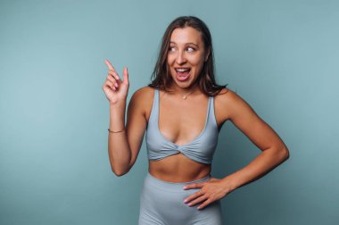 Aktif kıyafetli bir kadın mavi arka plana bakıp gülümsüyor..