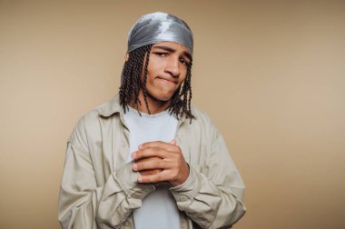 Saçları örgülü genç bir adam. Durag takıyor, düşünceli görünüyor..