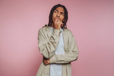 Saçları örgülü, pembe arka planı olan genç bir adam..