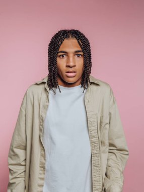 Saçları örgülü genç adam pembe arka plana şaşırmış görünüyor..