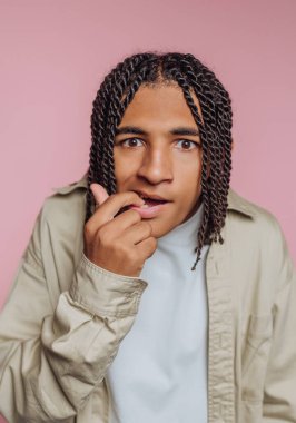 Saçları örgülü genç adam pembe arka plana şaşırmış görünüyor..